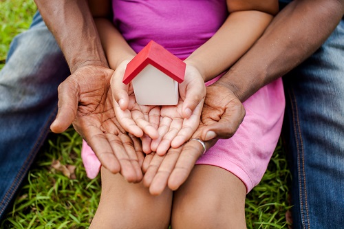 Hands of family together holding house in green park - family home and real estate concept